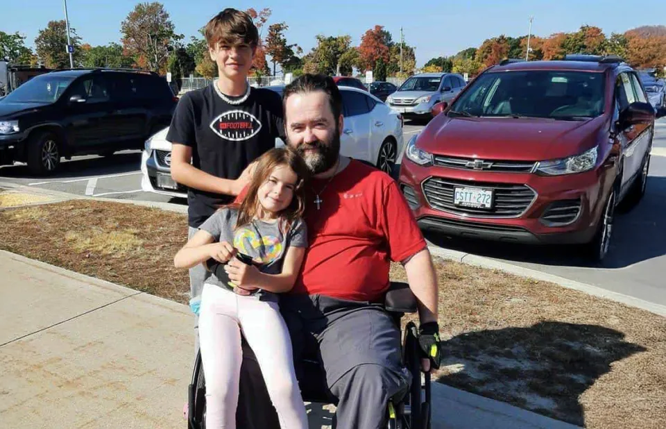 Corey Dunn sitting in a wheelchair being hugged by his family.