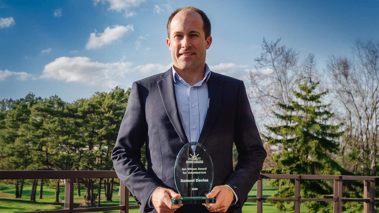 Sam Davies in a suit outside holding a UHKF Volunteer Award.