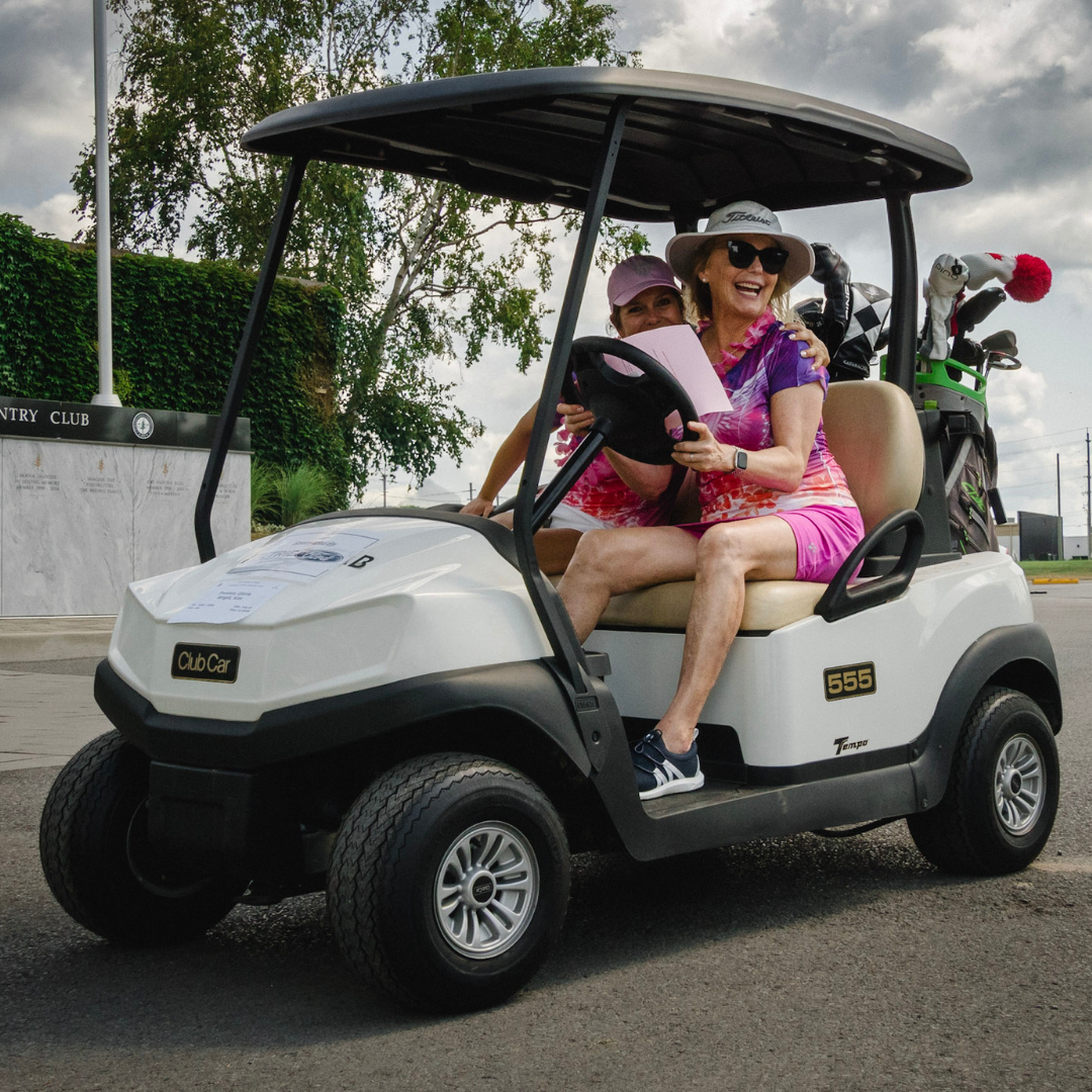 Women in pink smiling while driving a golf cart.