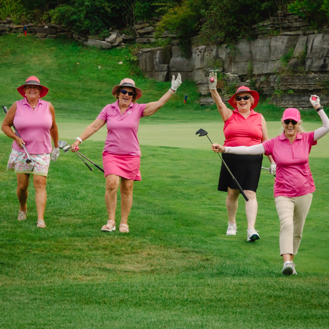 Women wearing pink golf outfits waving to the camera.