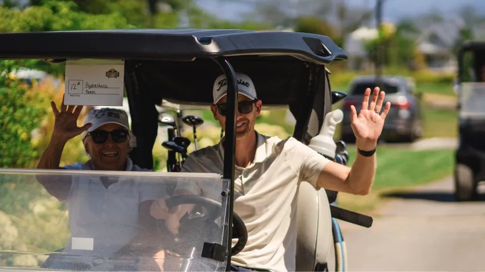 Golfers waving to the camera while driving pass on golf cart.