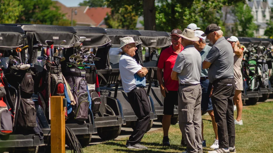 Group of men standing around golf carts laughing.