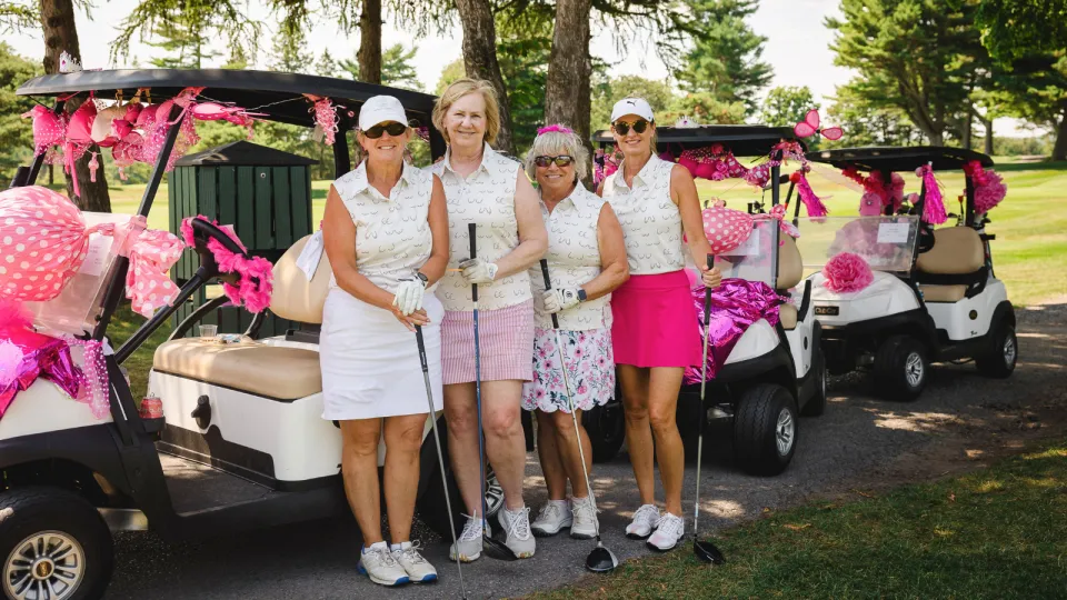 Golfers at the Rose of Hope Golf Tournament in pink golfing gear standing by their cart.