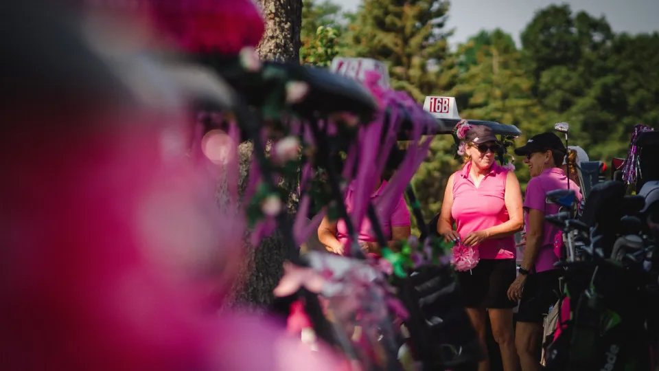 Golfers at the Rose of Hope Golf Tournament in pink golfing gear standing by their cart.
