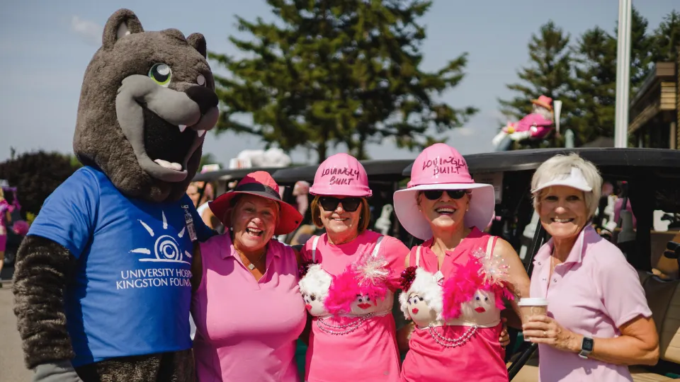 UHKF Mascot Asher with golfers at the Rose of Hope Golf Tournament in pink golfing gear.