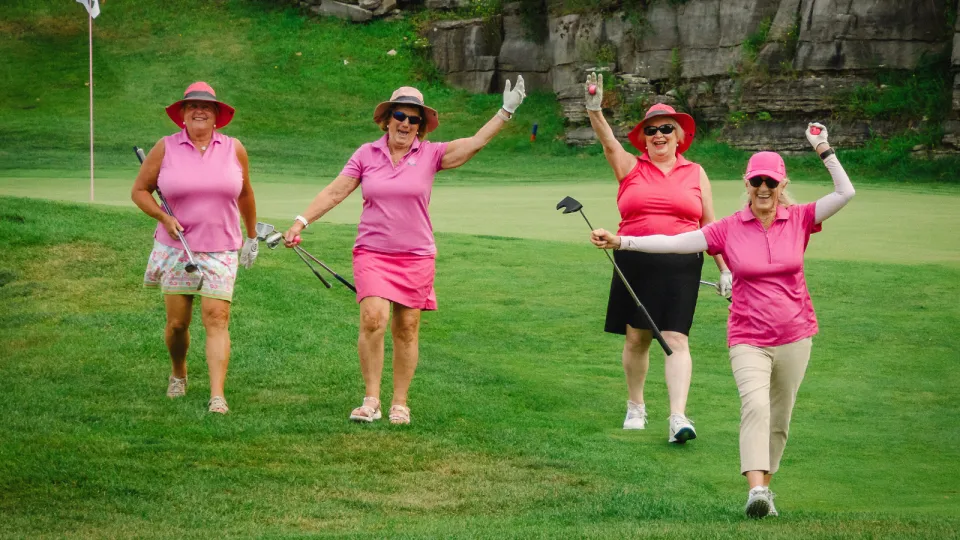 Golfers on the course at the Rose of Hope Golf Tournament smiling and waving at the camera.