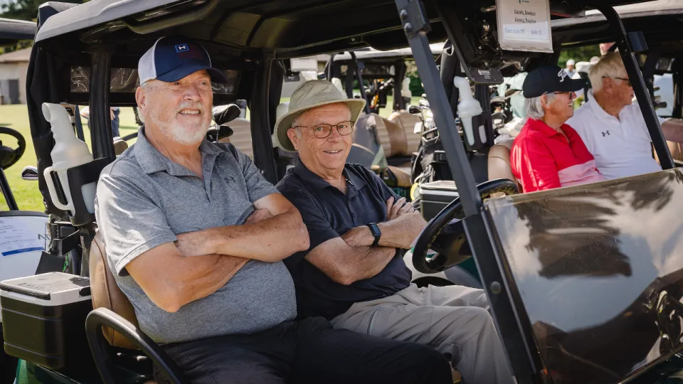 Two older male golfers smiling with their arms crossed in a golf cart.