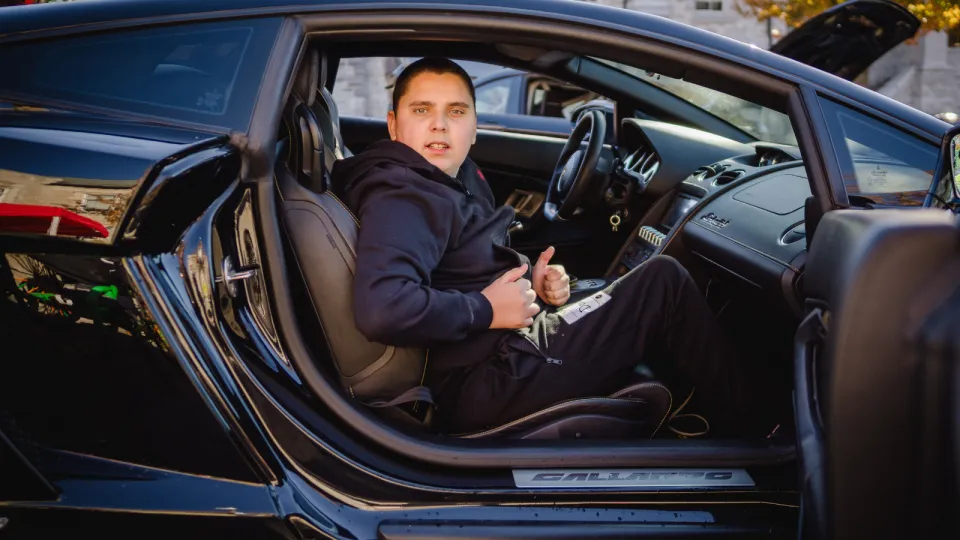 Child sitting and smiling behind the wheel of a super car