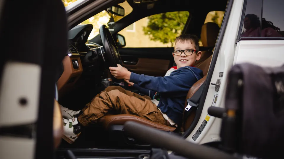 Child sitting and smiling behind the wheel of a super car