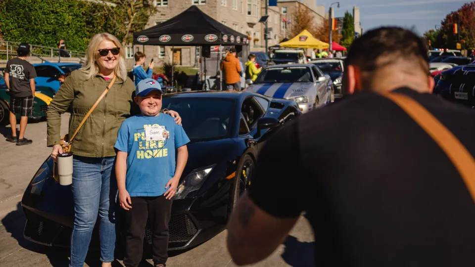 Families posing in front of super cars