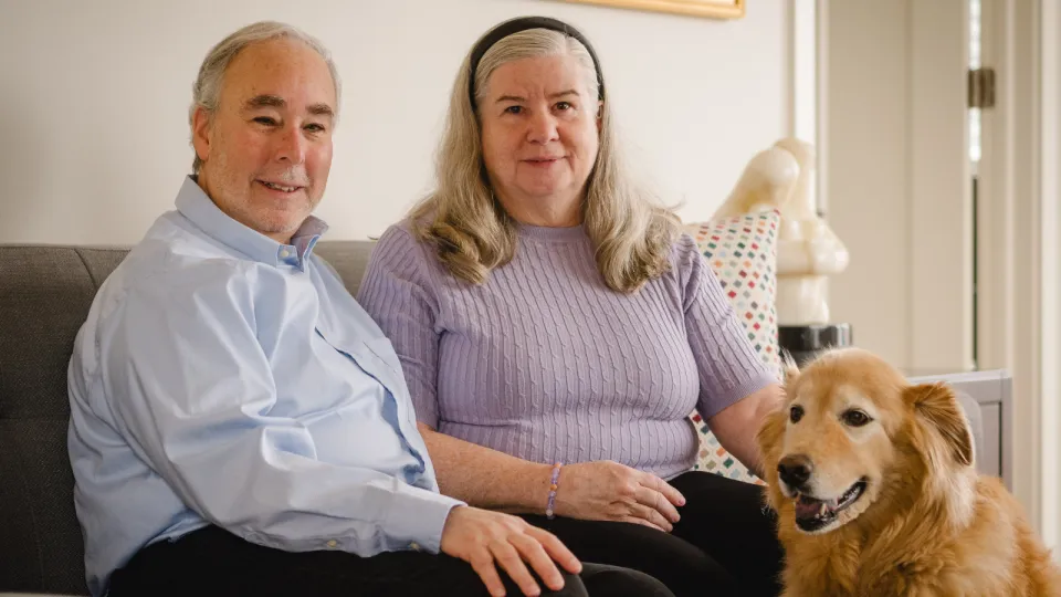 John and his wife sitting on their couch with their dog.
