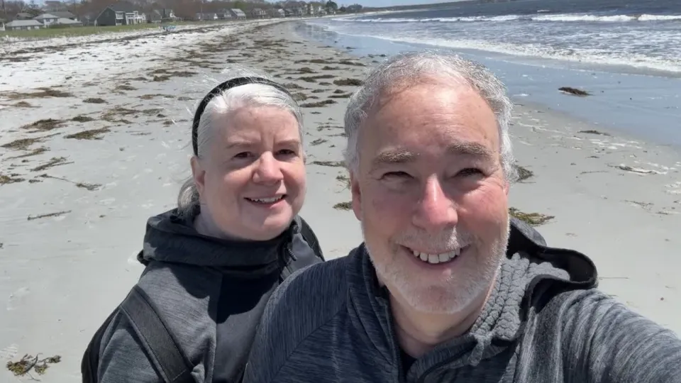 John and his wife smiling on the beach.