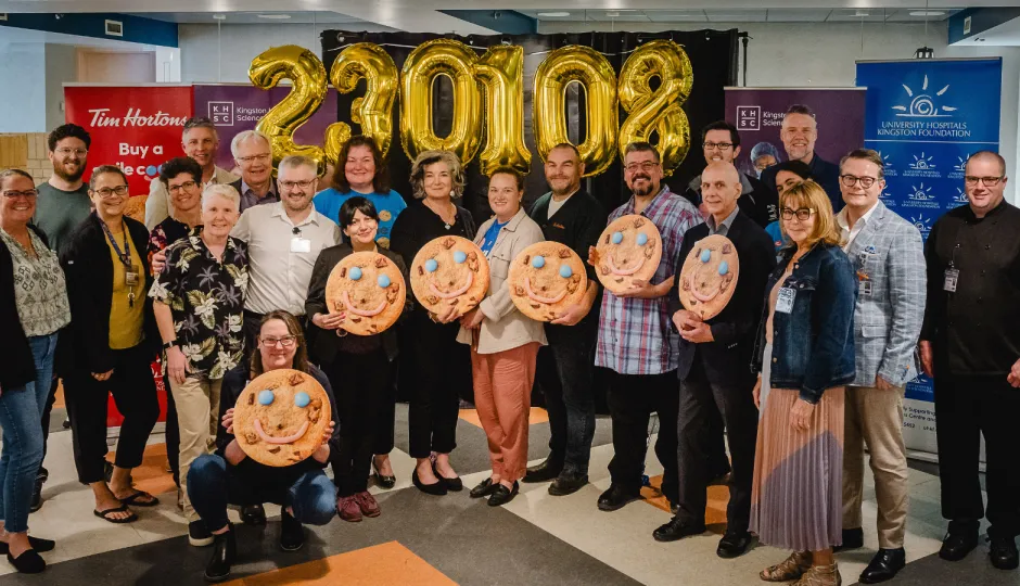 Smile Cookie Week funding announcement at Kingston General Hospital. Hospital and Tim Hortons staff holding smile cookies in front of number balloons.