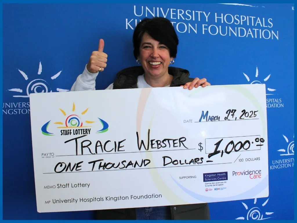 Tracie Webster holding $1000 big chq in front of blue UHKF background