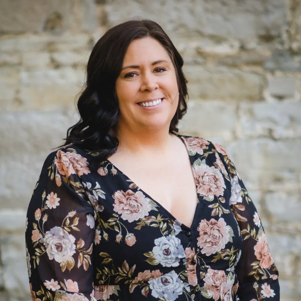 Krista Lessard smiling in a floral dress, standing in front of a brick wall.