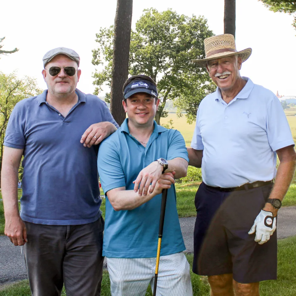 Three men in blue golfing shirts with clubs.