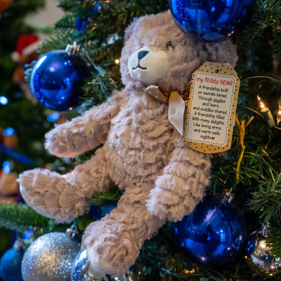 Picture of teddy bear sitting in the branches of a Christmas tree. 