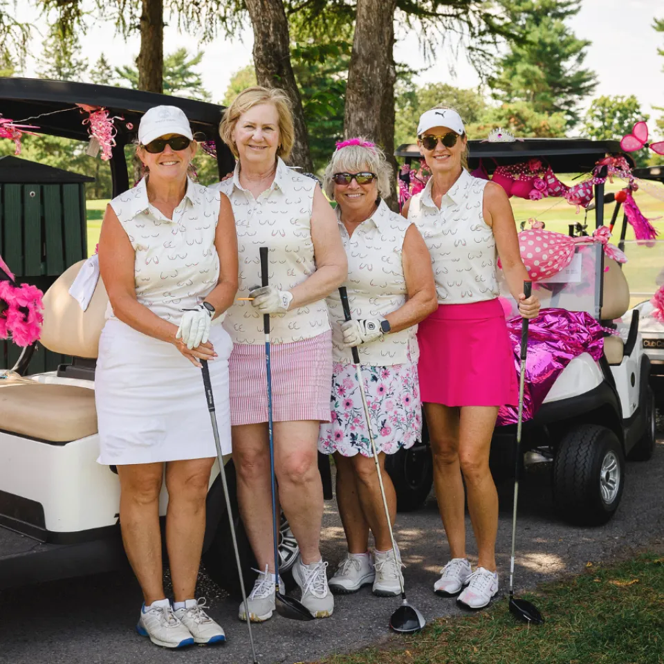Golfers at the Rose of Hope Golf Tournament in pink golfing gear standing by their cart.